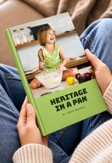 Hands holding a green Heritage in a Pan cookbook