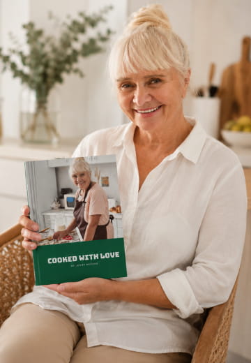 Woman holding a green TableTales cookbook titled Cooked with Love