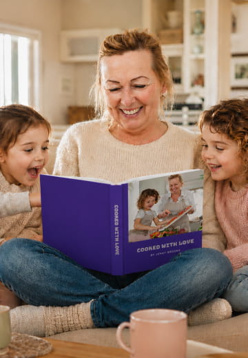 Grandmother and grandchildren reading a purple Cooked with Love cookbook