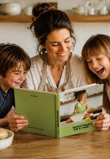 Mother and children laughing over an open Heritage in a Pan cookbook